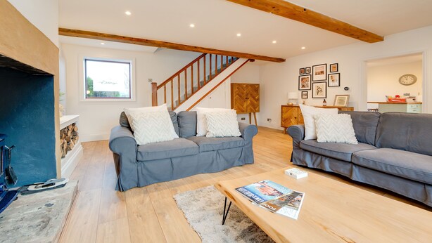 A spacious living room with two grey sofas, wooden beams on the ceiling, a staircase, and a fireplace. - Canal side cottage with hot tub, sky tv and log fire (Lathom)