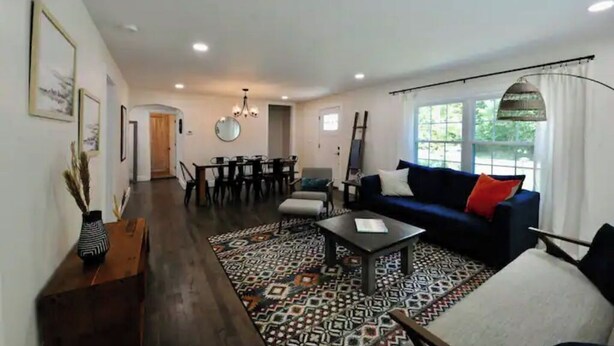 Un salon spacieux avec un canapé bleu foncé, un tapis à motifs et un coin repas agrémenté d’un lustre.