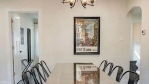 Un coin repas avec une table en bois et des chaises noires, un lustre et un tableau encadré au mur.