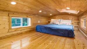 Une pièce chaleureuse, aménagée dans un chalet en bois, avec un lit, une fenêtre et une lucarne.