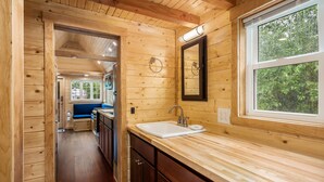 L’intérieur d’une cabane en bois comprend un coin cuisine équipé d’un évier, de placards et d’une fenêtre.
