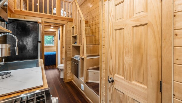 Un intérieur de cabane en bois, de taille réduite, comprenant un coin cuisine, une salle de bain et une chambre en mezzanine.