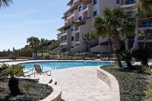 A swimming pool with lounge chairs, palm trees, and a multi-story building in the background. - Sandcastle Court #275 -Kitchen (Nassau County)