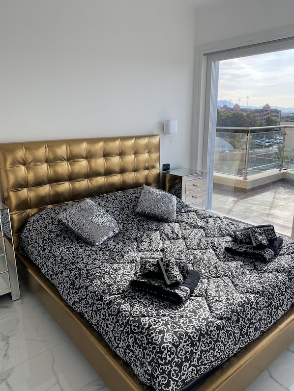 A bedroom with a gold headboard, patterned bedding, and a view of a parking area through a glass door.