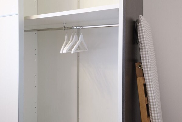 A white closet with a hanging rod and a checkered cloth draped over a wooden hanger.