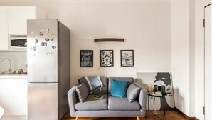 Ett modernt kök med ett inbyggt kylskåp, en grå soffa med kuddar och ett litet sidobord med en lampa.