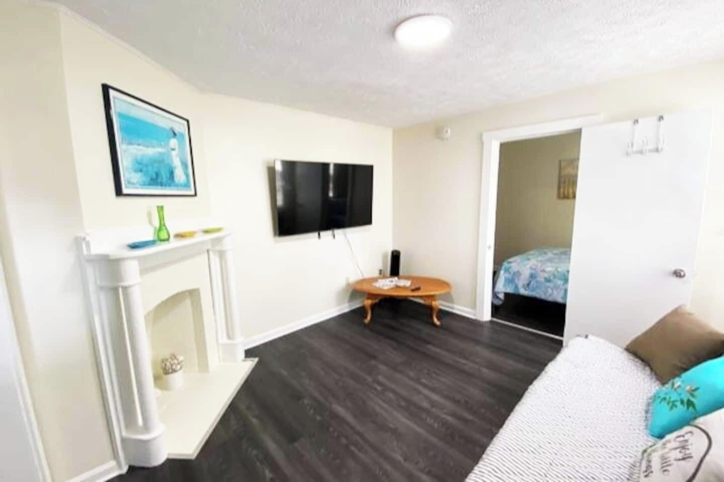 A room with a fireplace, a flat-screen TV, a bed with a blue bedspread, and a door leading to another room.