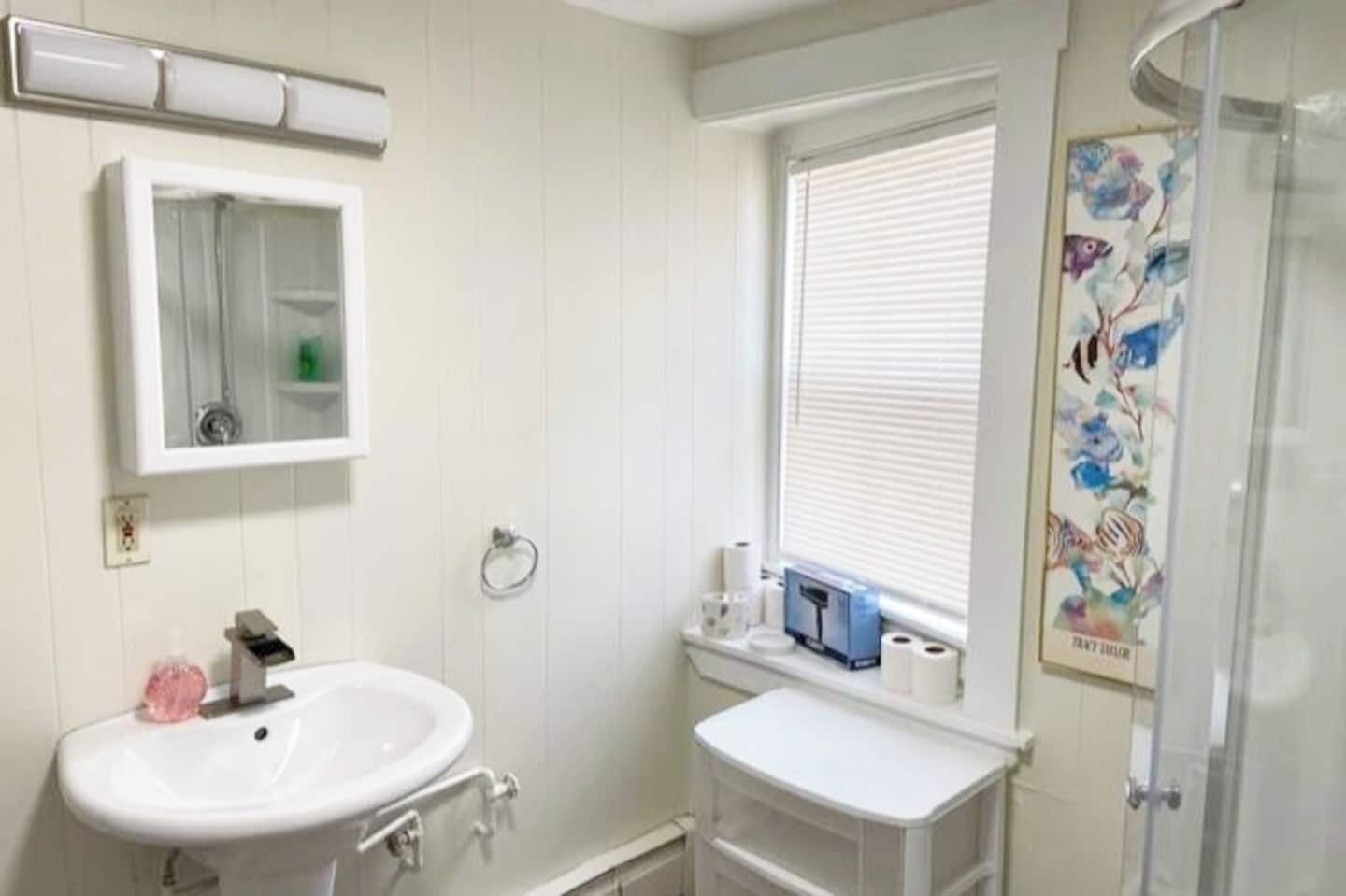 Ein Badezimmer mit Waschbecken, Spiegel, Fenster und Dusche.