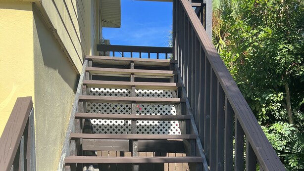 Una escalera de madera con barandilla de metal que lleva a un porche cubierto.