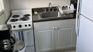 Una cocina con armarios blancos, estufa, pileta y refrigerador.