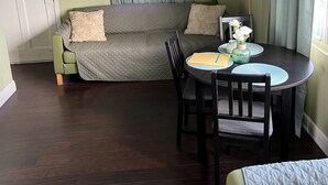 Una habitación con un sofá verde, una mesa redonda de comedor con sillas, una lámpara y una ventana con cortinas.