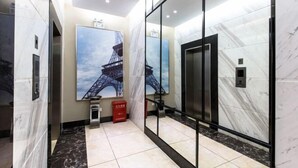 Een modern liftgedeelte met marmeren wanden, een groot schilderij van de Eiffeltoren en een rode prullenbak.