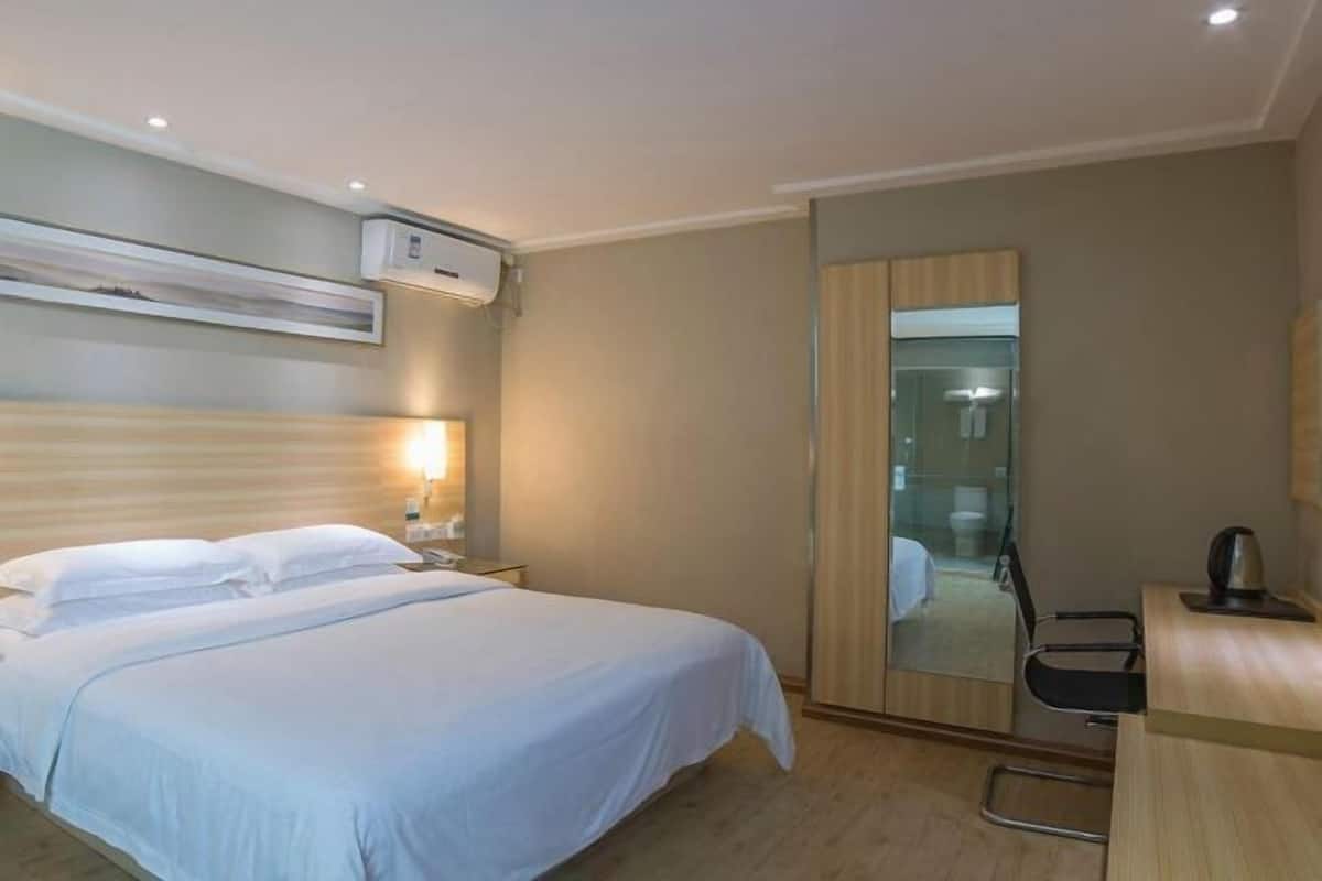 Une chambre d’hôtel comprenant un lit, une table de chevet, une lampe, un miroir et un bureau avec une chaise.