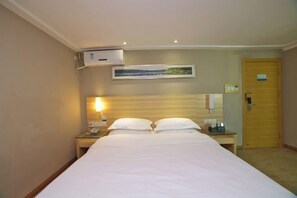 Quarto de hotel com cama, mesa de cabeceira com abajur, aparelho de ar condicionado, quadro pendurado na parede e porta de madeira.