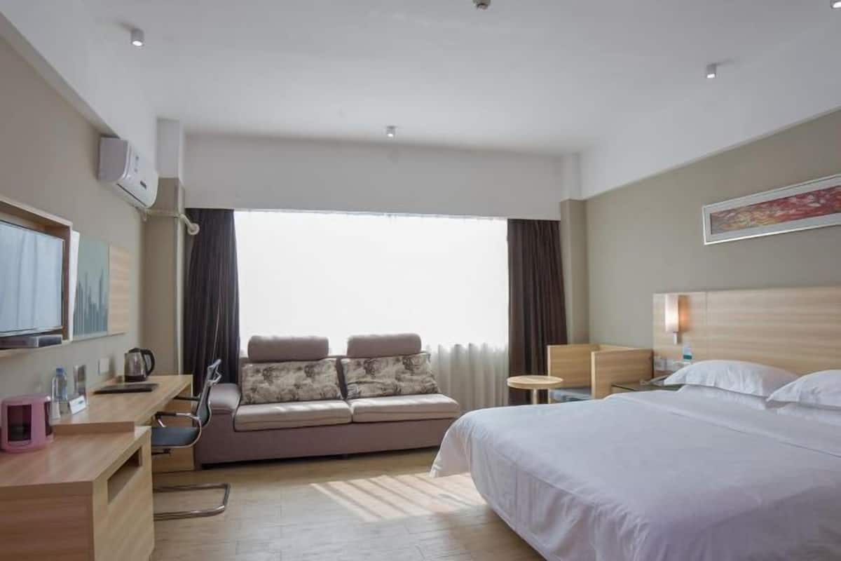 Une chambre d’hôtel avec un lit, un canapé, un bureau, une télévision et une fenêtre avec des rideaux.
