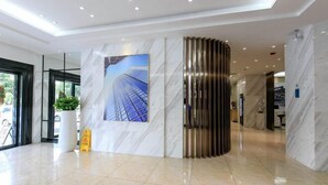 Een moderne hotel lobby met een marmeren wand, een groot gepoft beeld van een gebouw en een strakke, metalen scheidingswand.