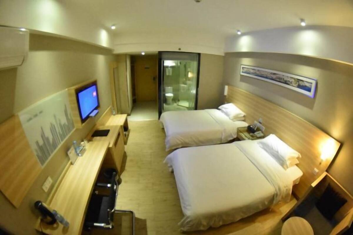 Une chambre d’hôtel équipée d’un bureau, de deux lits, d’une télévision et d’une salle de bain visible à travers une porte en verre.