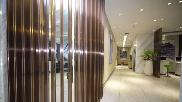 Een moderne hotelgang met een glanzende metalen scheiding, een receptiebalie met een plant en een schone betegelde vloer.