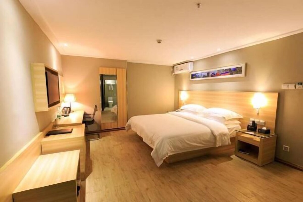 Quarto de hotel com cama, mesa de cabeceira, luminária e ar-condicionado fixado na parede.