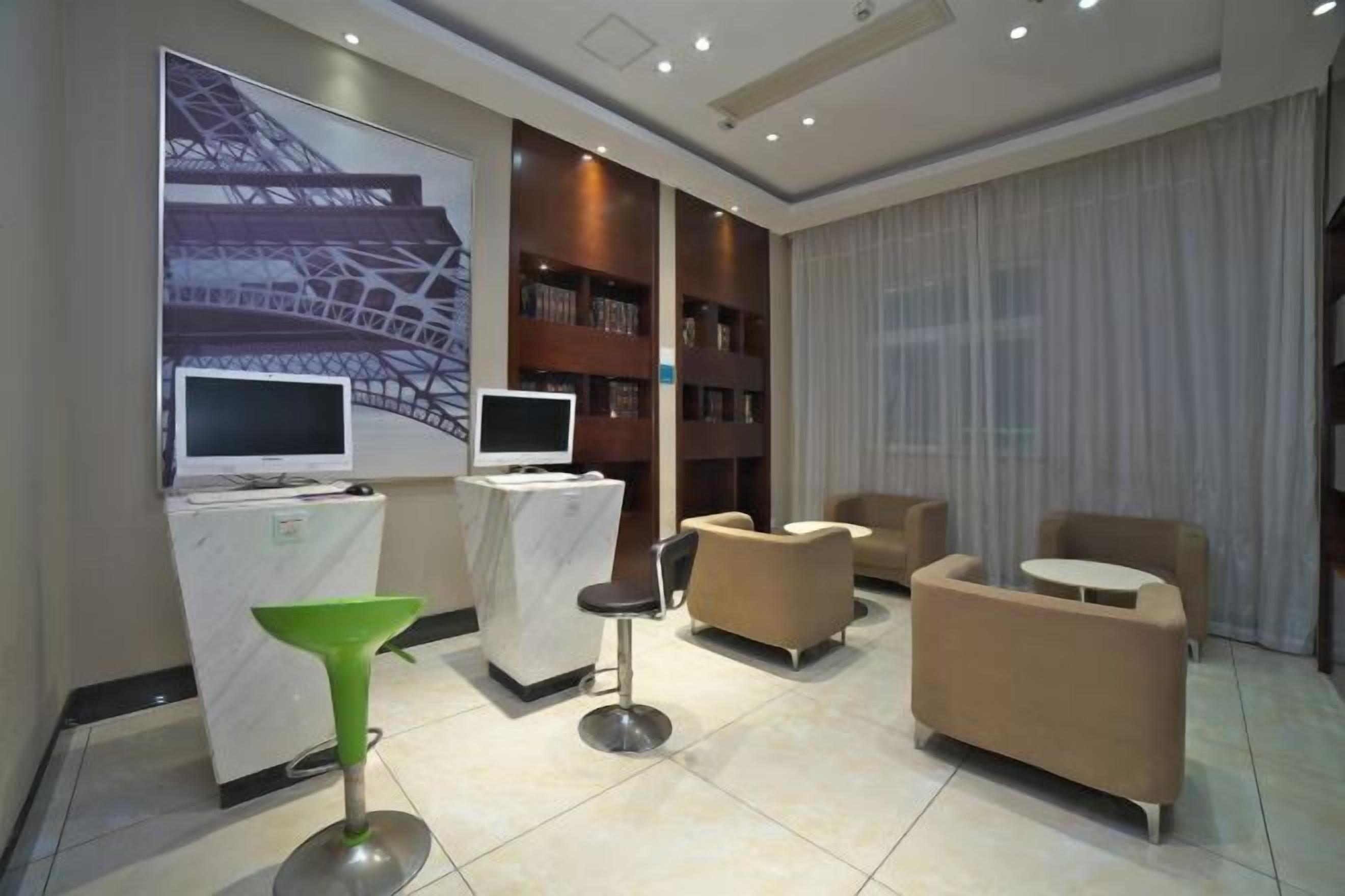 A modern hotel lobby with a large screen displaying a cityscape, a reception desk, a green bar stool, and comfortable seating areas.