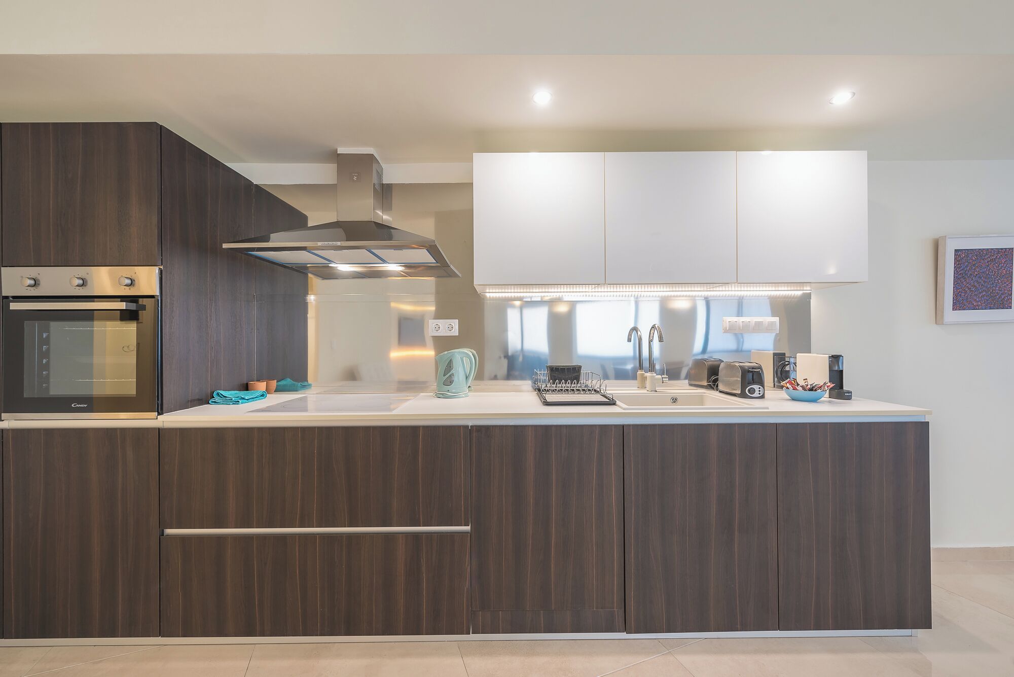 A modern kitchen with dark wood cabinets, a built-in oven, a stainless steel range hood, and a white countertop.