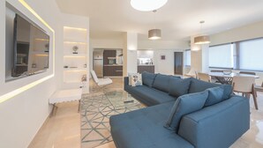 A modern living room with a sectional sofa, a glass coffee table, and a dining area with a table and chairs. - KYPSELI PLATINUM (Athens)