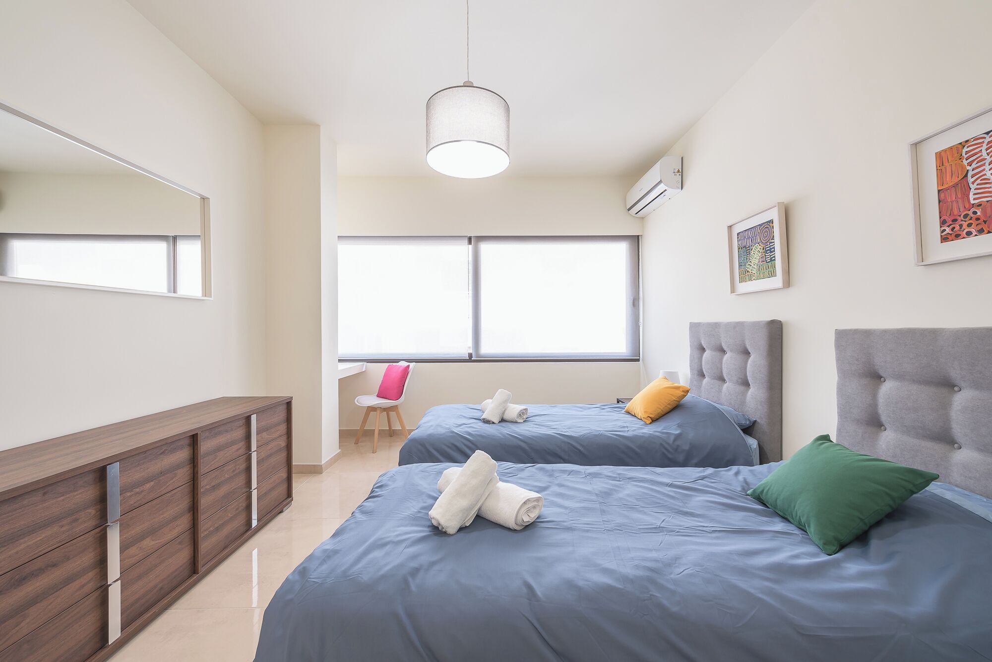 A modern bedroom with two beds, a desk, and a chair.