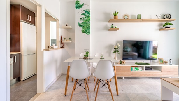 A modern kitchen with white cabinets and a built-in refrigerator. There is a dining table with white chairs and a TV on a wooden stand. - Apartment in Rota-Cádiz, new and modern near the beach. (Rota)