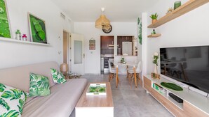 A modern living room with a sofa, coffee table, TV, and kitchen in the background. - Apartment in Rota-Cádiz, new and modern near the beach. (Rota)