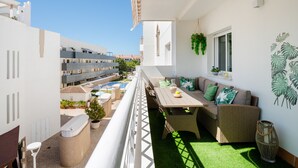 A balcony with a dining area, seating, and a view of a swimming pool and buildings. - Apartment in Rota-Cádiz, new and modern near the beach. (Rota)
