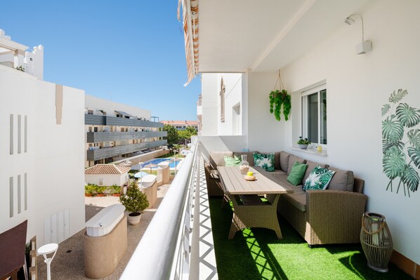 A balcony with a dining area, seating, and a view of a swimming pool and buildings. - A new, modern apartment in Rota (Cádiz), located near the beach. (Rota)