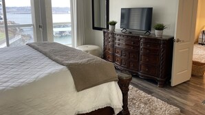 A bedroom with a large bed, a dresser, a television, and a view of a body of water through a sliding door. - Updated Lands End Upscale Condo - Sleeps 9 (Osage Beach)