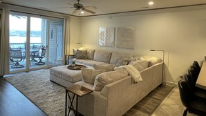 A living room with a sofa, a coffee table, and a ceiling fan. There is a sliding glass door leading to an outdoor area with a table and chairs. - Updated Lands End Upscale Condo - Sleeps 9 (Osage Beach)