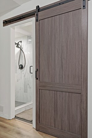 Une pièce dotée d’une porte coulissante donnant accès à un espace douche avec une porte en verre et un pommeau de douche.