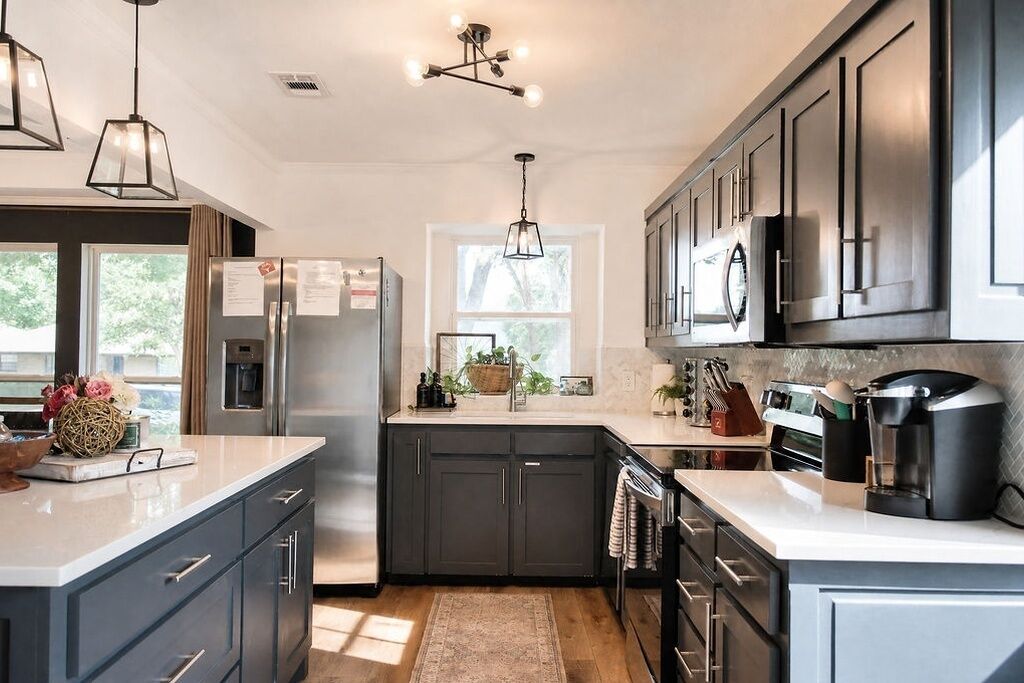 A modern kitchen with dark cabinets, stainless steel appliances, and pendant lighting.