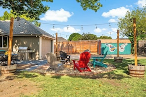 Patio trasero con mobiliario exterior, una parrilla y una chimenea decorativa.