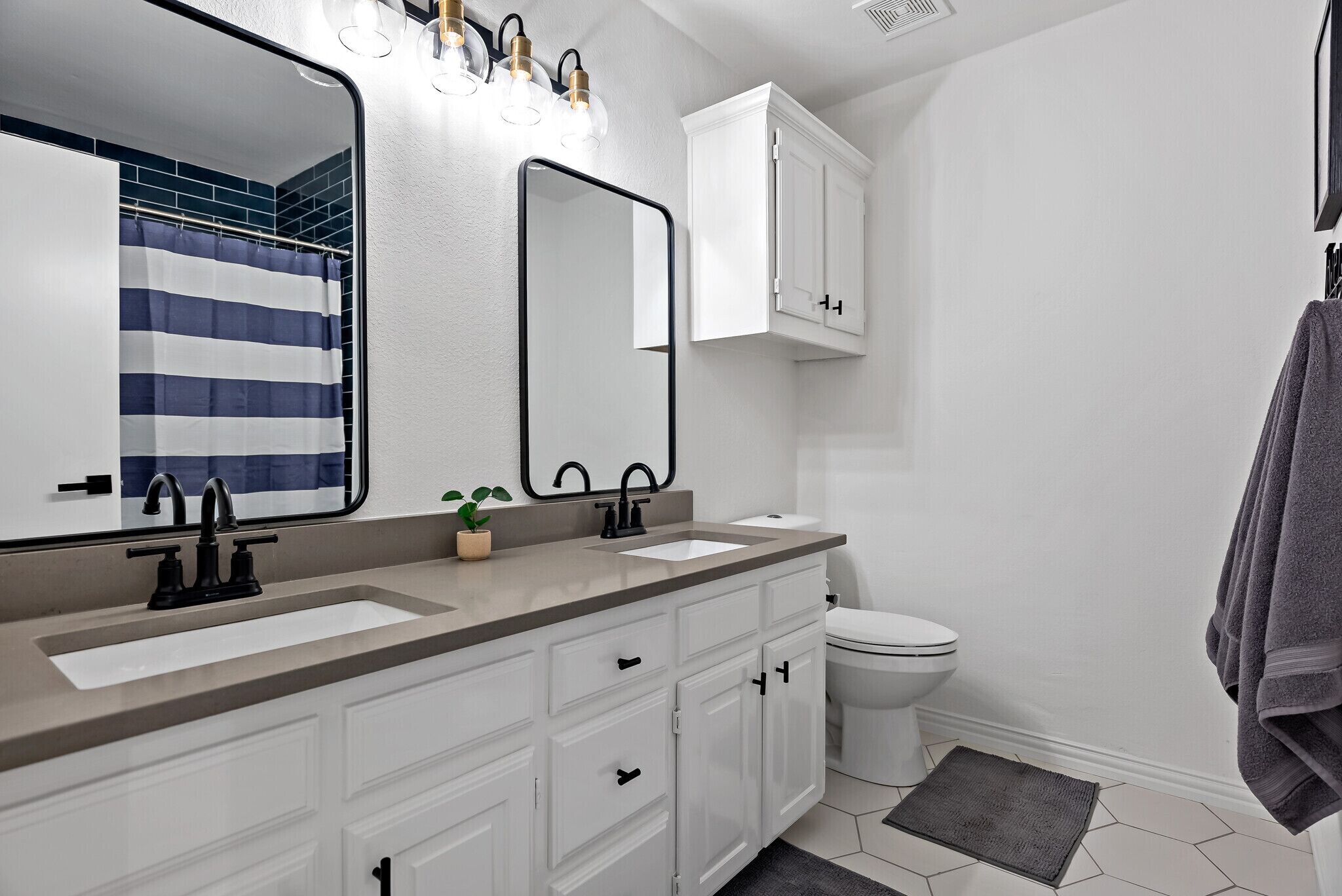 A modern bathroom with a large mirror, two sinks, a toilet, and a shower curtain.