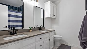 A modern bathroom with a large mirror, two sinks, a toilet, and a shower curtain.