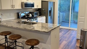 A kitchen with a large island, bar stools, a stainless steel refrigerator, and a sign that reads 'BEACH HOUSE'. - Winter Rates at Seize the Bay (Port St. Joe)