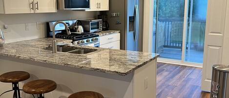 Una cocina con una isla grande, taburetes de bar, un refrigerador de acero inoxidable y un cartel que dice 'BEACH HOUSE'.
