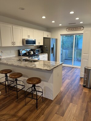 A kitchen with a large island, bar stools, a stainless steel refrigerator, and a sign that reads 'BEACH HOUSE'. - Winter Rates at Seize the Bay (Port St. Joe)
