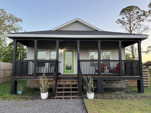 A two-story house with a porch, a green door, and a small garden with potted plants. - Winter Rates at Seize the Bay (Port St. Joe)