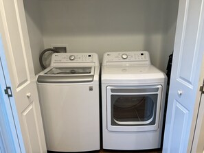 A laundry room with two white appliances, one front-loading and one top-loading, with a door on the left. - Winter Rates at Seize the Bay (Port St. Joe)