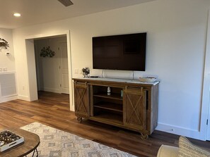 A living room with a flat-screen TV mounted on the wall, a wooden cabinet with open shelves, and a patterned rug on the floor. - Winter Rates at Seize the Bay (Port St. Joe)