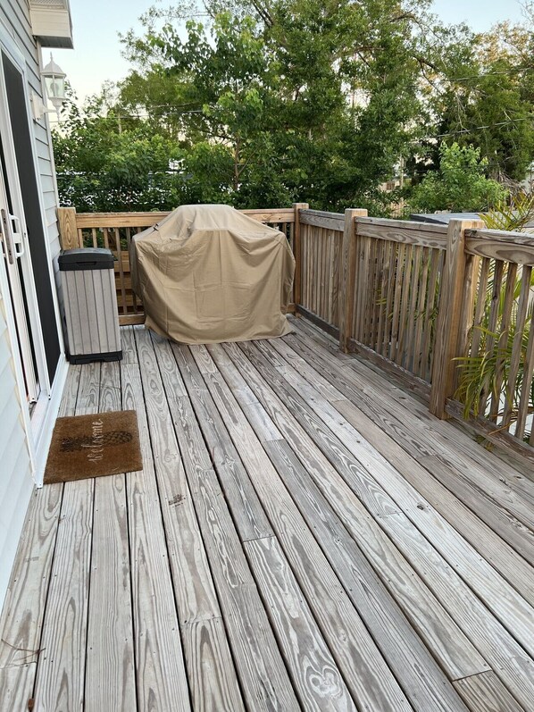 A wooden deck with a covered grill, a trash can, and a doormat. - Winter Rates at Seize the Bay (Port St. Joe)