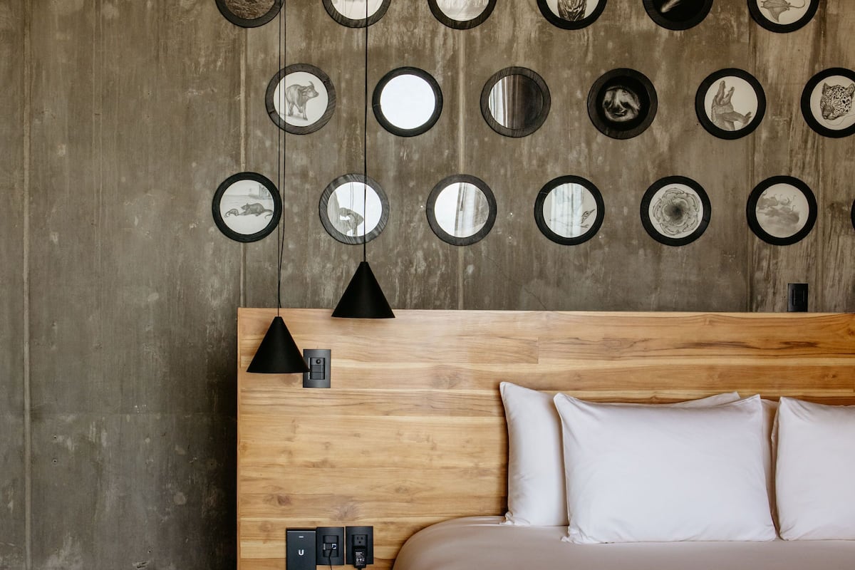 Un dormitorio moderno con cabecera de madera, cama con ropa de cama blanca y una pared decorada con espejos circulares.