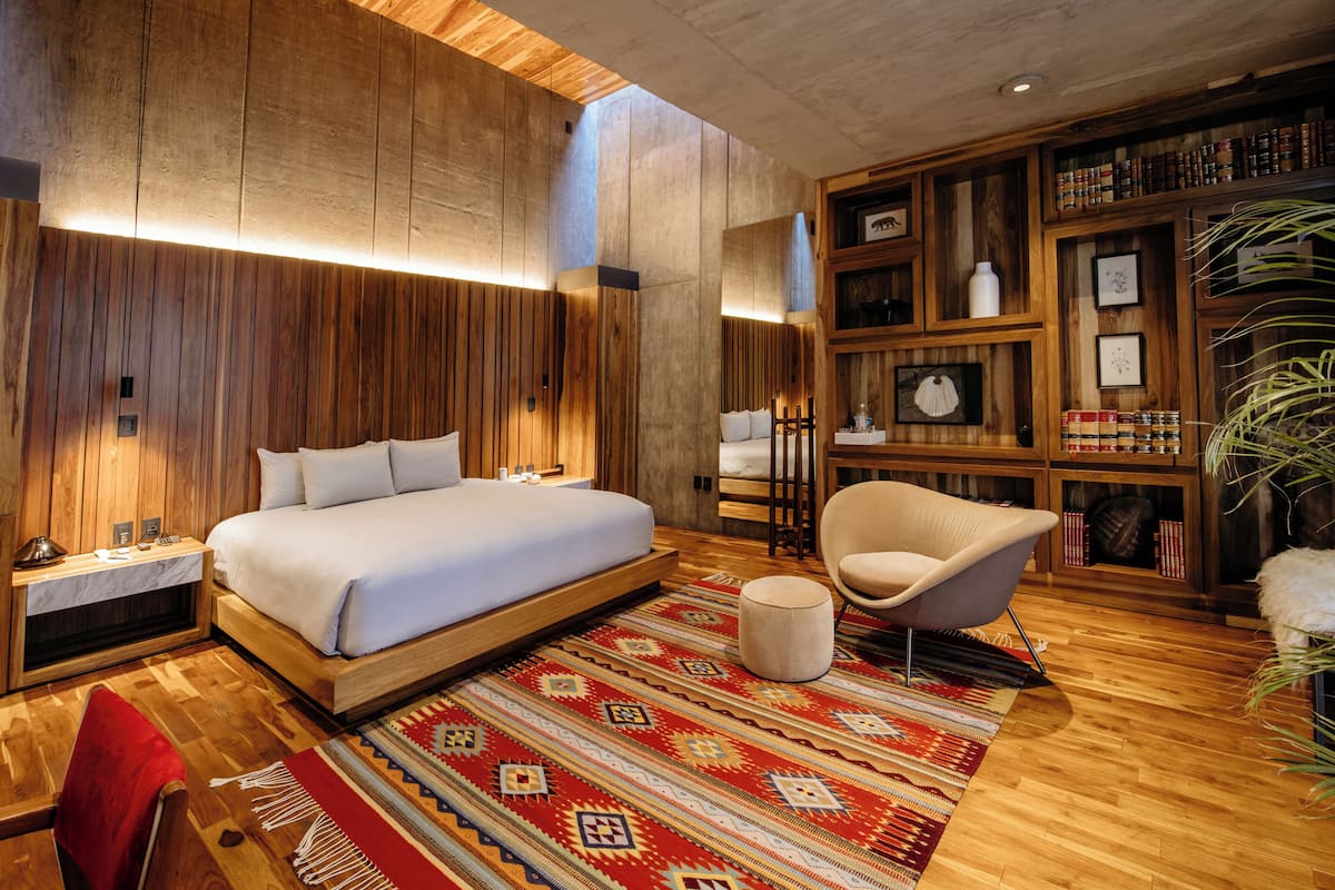 Un dormitorio moderno con una cama grande, una silla, una estantería y una alfombra estampada.