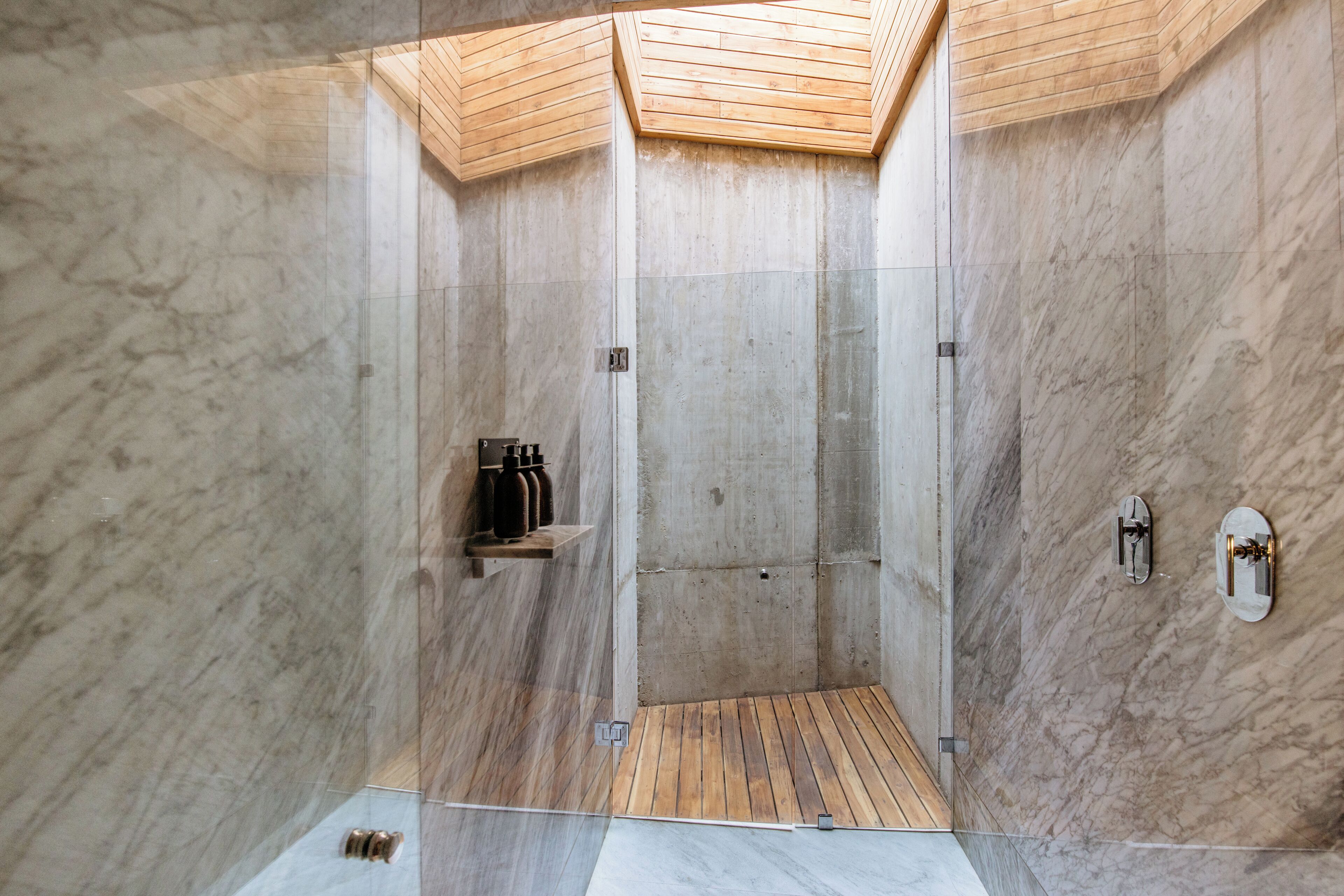 A modern shower with a wooden ceiling and marble walls.