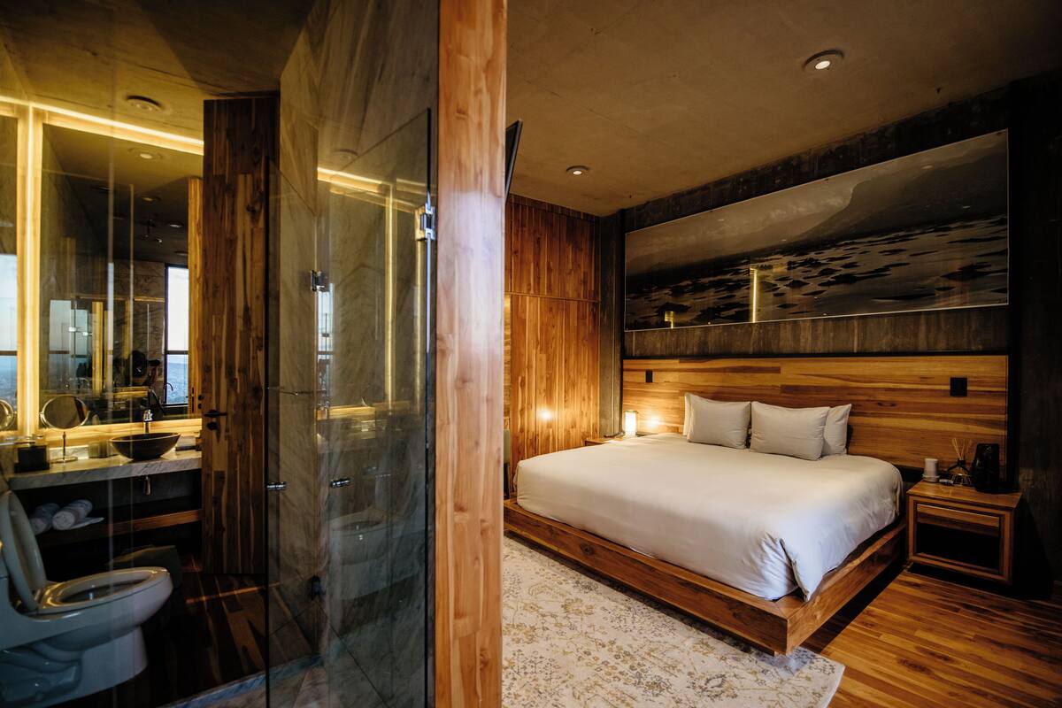 Un dormitorio moderno con una cama grande, paneles de madera, cabina de ducha de vidrio y un espejo amplio.