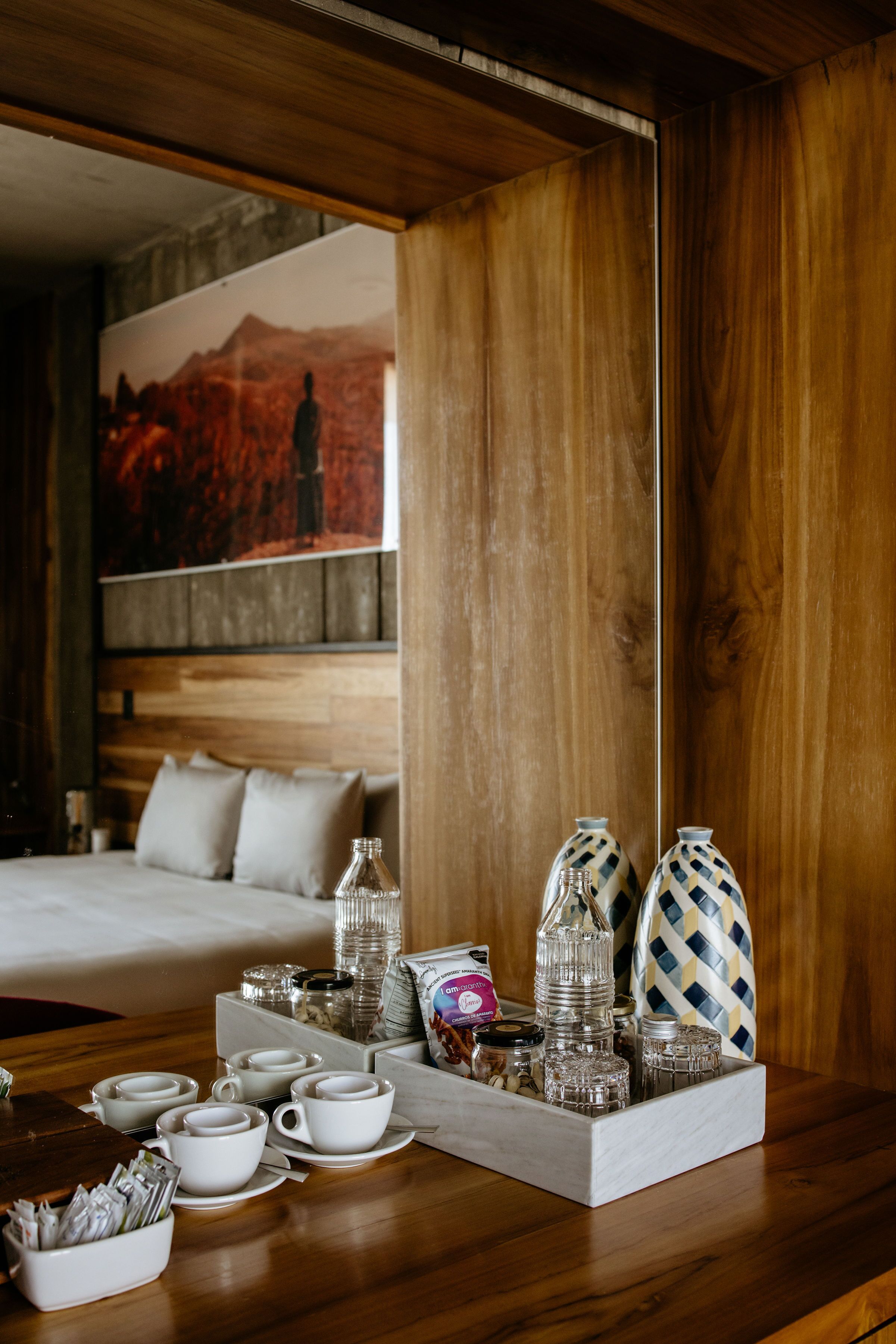 Una habitación de hotel con cabecera de madera, cama con ropa de cama blanca, una mesa de comedor con vajilla y un cuadro en la pared.